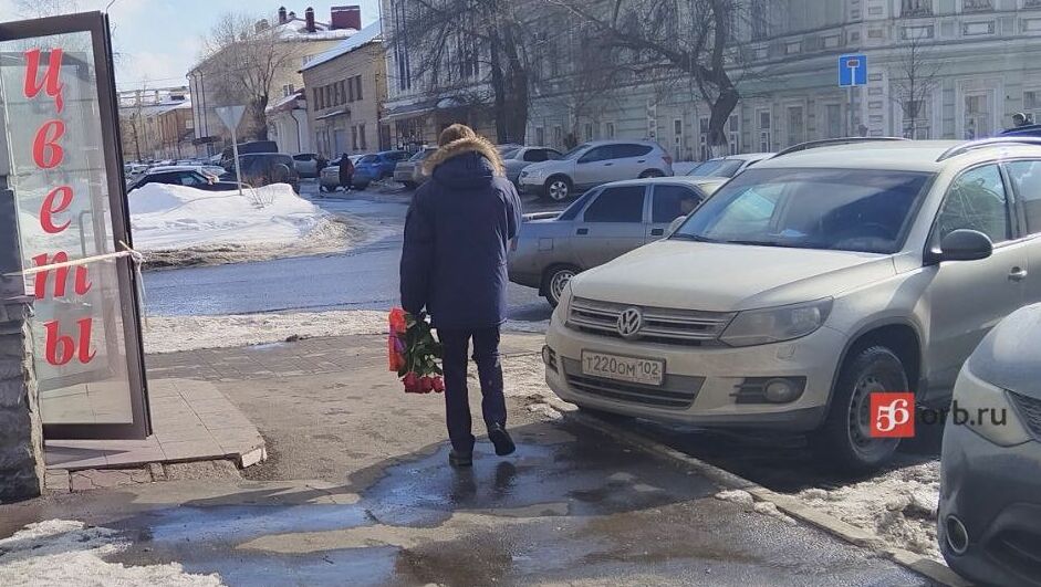 Мужчина несет только что купленный букет красных роз и подарок в красивом пакете